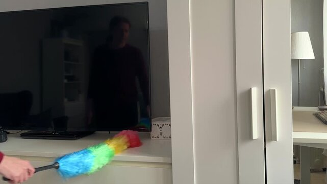 Woman dusts dresser surface with feather duster closeup zoom in