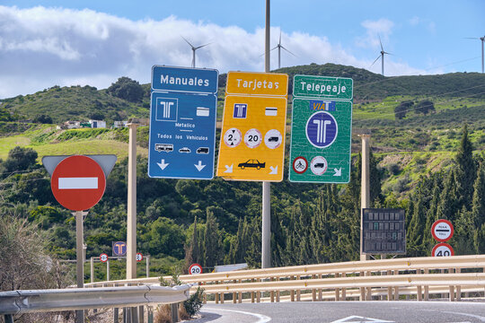 Manilva, Spain - 18 February 2026: View of the vibrant toll signs set against the undulating green hills and wispy clouds, creating a striking contrast of manufactured order and natural beauty.