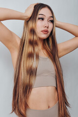 Obraz premium Young woman with long straight hair posing with hands on head in studio. Beauty, fashion, style, casual outfit, and natural makeup on female model.