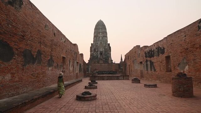 Ayutthaya, Thailand- 25th february, 2024: Female traveler in hat stands between brick walls at Wat Ratchaburana, Ayutthaya, watching ancient prang tower at sunset, Thailand heritage tourism concept