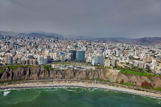 aerial photograph showcasing the unique architecture of the Larcomar shopping mall, built directly into the cliffs of the Costa Verde. The image captures the dense urban landscape of the Miraflores