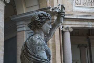 Naklejka premium Detailed close up: A classical marble statue or sculpture of a woman holding a scroll stands in an ancient Roman temple. 