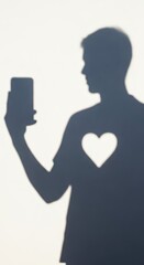 Silhouette of a person holding a mobile device casting a shadow with a heart shape on the chest