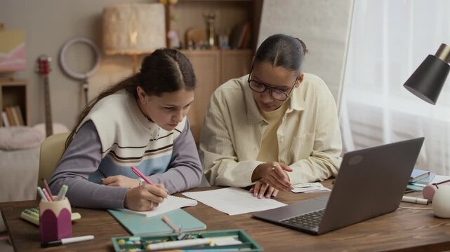 Medium shot of tutor and student sitting at desk and looking at paper with exercises, woman communicating with student