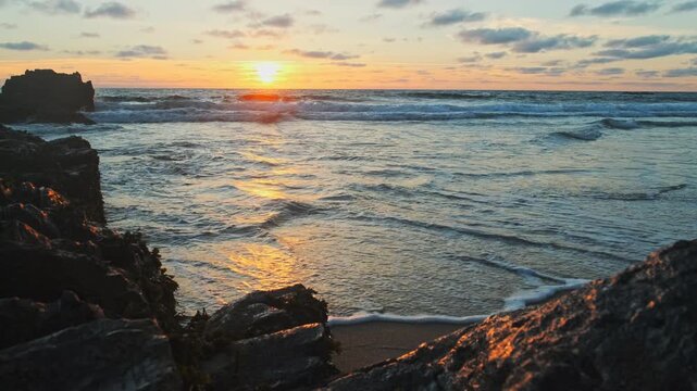Beautiful natural landscape with sandy beach  with big stones during sunset.  Slow motion - rolling ocean waves to the rocky shore while sunset.  Popular summer tourist destination in Portugal. Travel