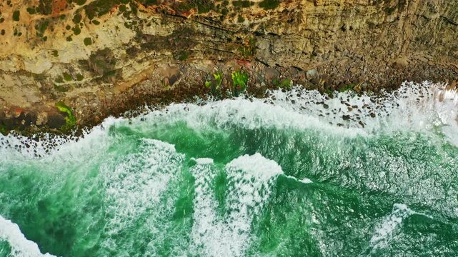 Drone view over ocean and shore with stones, on summer sunny day.  Ocean waves break on the rocky shore, on sunny summer day. Top view to the beautiful landscape with sea shore.  4k footage.