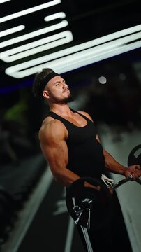Focused athlete performing standing barbell biceps curls in a dimly lit gym, showcasing a muscular physique, arm strength, and concentration during a demanding training session.
