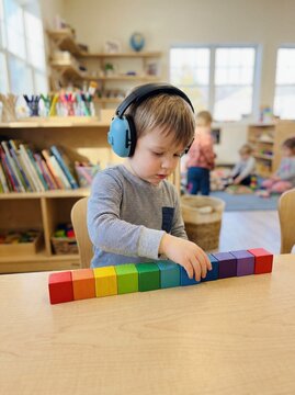 Autism Spectrum: Professional photography, a child wearing noise-canceling headphones in a bright classroom, stacking toys in a perfect line, soft focus background, authentic.