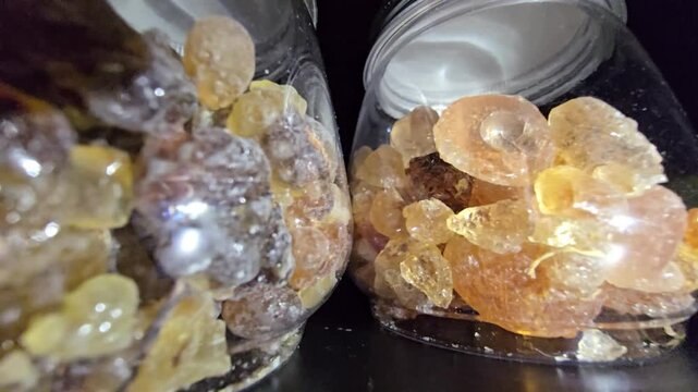 Close-up of glass jars containing high-quality Gum Arabic and Frankincense (Luban) crystals. The shot highlights the organic texture and amber-gold transparency of these natural resins.