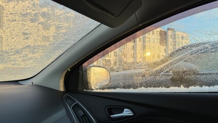 Fototapeta premium Interior view of a car with a frozen windshield and side window parked on a snowy city street