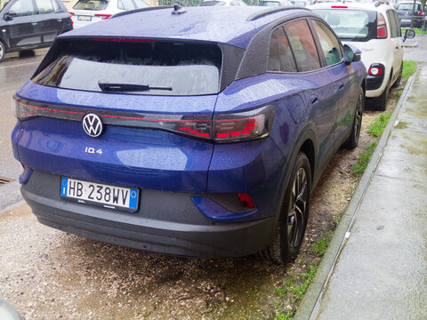 A rear view of a vibrant blue Volkswagen ID.4 electric SUV parked curbside on a rainy day, showcasing its modern design and taillights