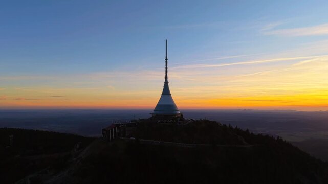 Watch as the sun sets over Jested Mountain in Czechia. The transmitter shines against the colorful sky. This spot near Liberec is known for stunning views and a hotel.