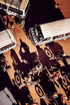 Kampala, Uganda - 28 March 2024: View of a vibrant street scene with parked motorbikes and white vans casting long shadows under the harsh sunlight.