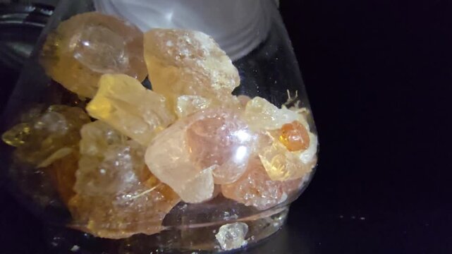Close-up of glass jars containing high-quality Gum Arabic and Frankincense (Luban) crystals. The shot highlights the organic texture and amber-gold transparency of these natural resins.
