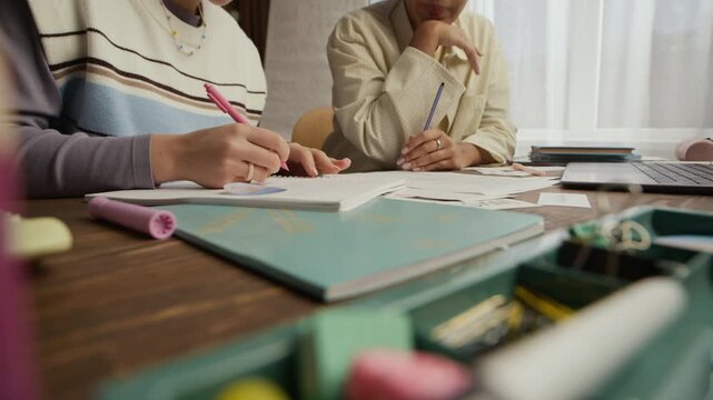 Unrecognizable teen student writing in notebooks while her female tutor explaining task