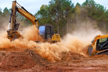 Construction skid steer equipment, excavator digs into ground, kicking up dust at site preparation land development. © ungvar