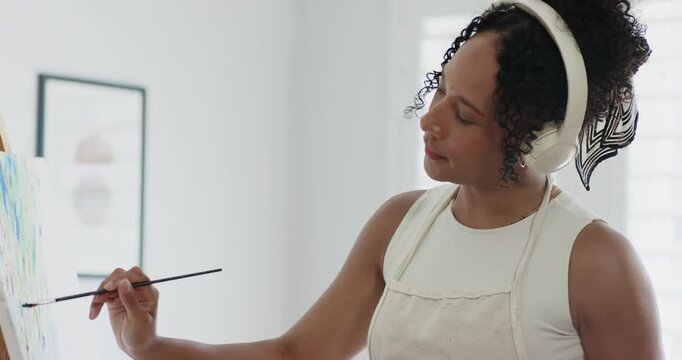 African American woman raising brush to canvas at studio, painting blue marks with apron, refining