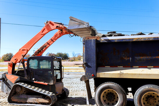 Construction bobcat machine loads soil into dump truck at work site under construction works
