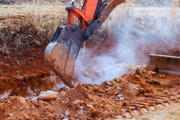 Excavator operates on dirt path, removing soil in ground during digging trench work © ungvar