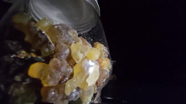 Macro video of high-quality raw Frankincense (Luban) crystals in a glass jar. The shot captures the natural organic texture and the beautiful translucent amber and golden hues of the resin.