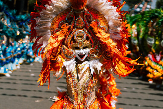 Cebu City, Philippines - 18 January 2026: View of a vibrant Sinulog festival performer, adorned in fiery orange and white feathers, dances with a captivating white mask.