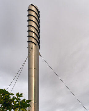 Nymolla, Sweden - 21 September 2025: View of a stainless steel chimney structure ascending skyward, spiraling upwards with dark accents against a soft, overcast sky.