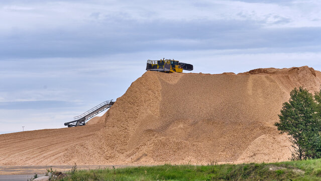 Nymolla, Sweden - 21 September 2025: View of a colossal mountain of wood chips, crowned by a special bulldozer, under a muted sky.