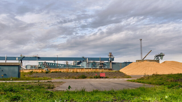 Nymolla, Sweden - 21 September 2025: View of the Sylvamo Nymolla Mill, where steel structures meet a vast mound of raw wood chip material under a sky streaked with grey.