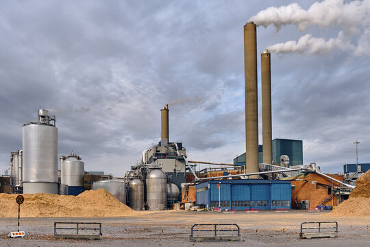 Nymolla, Sweden - 21 September 2025: View of Sylvamo Nymolla Mill, its towering chimneys releasing plumes of smoke into the expansive sky above. Heaps of saw dust ready to be processed.