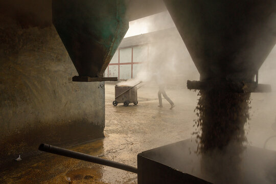 Ashuganj, Bangladesh - 15 January 2021: View of steaming industrial machinery casting long shadows as a worker transports goods in the factory.