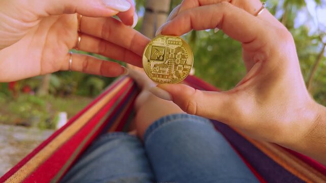 First Person Perspective Holding Golden Bitcoin Coin While Resting in Hammock Among Palm Trees Showing Digital Gold Financial Independence and Modern Wealth