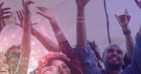 Raising friends' arms while holding clear cups under canopy, wearing floral headband and wristbands