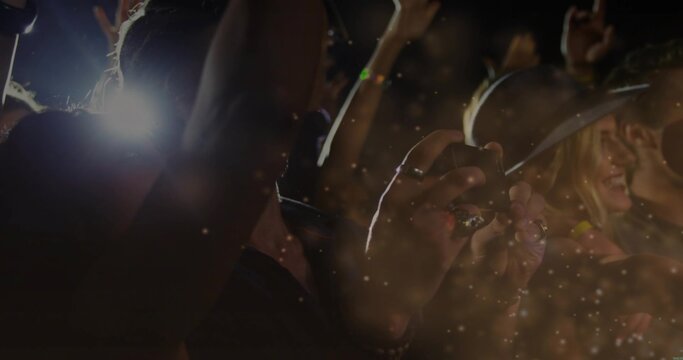 Holding smartphone, hands recording concert at venue, showing camera flashes, brimmed hat, haze