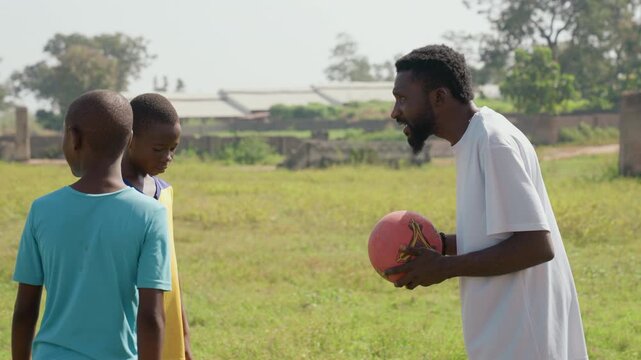 Black mentor persuades kids with ball, sunlit grass field, african boys and girl listen intently, coach offers tryout invitation, serious tone and life lesson exchange, grassroots sport scene,
