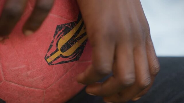 Closeup hand near red ball emblem, confident touch from player on bench, logo detail and textured rubber surface, steady fingers preparing for play with poised control and intent