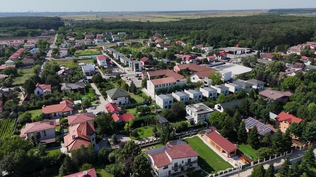 Cinematic drone aerial over Corbeanca near Bucharest, Romania, showing modern houses and villas, residential streets and green gardens at the edge of a dense forest.