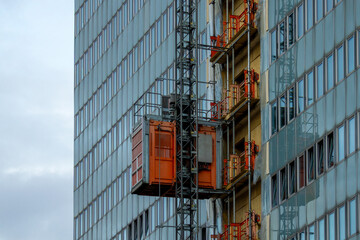 Orange construction hoist on a modern glass skyscraper in Oslo Norway. Industrial elevator for high rise building renovation and urban development project in the Norwegian capital. © photoopus