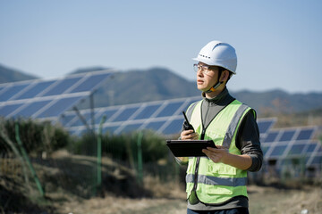 Engineer inspecting a photovoltaic power station on-site while holding a tablet and walkie-talkie