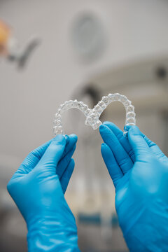 Dental professional holds clear aligners in hands during orthodontic treatment session at clinic
