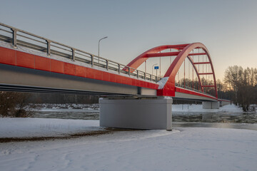 Amidst a snowy landscape, the striking red truss bridge gracefully arches over the San River in Gmina Ulanow, Podkarpackie Voivodeship, Poland