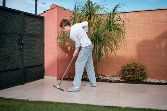 Teenager boy cleaning patio with a squeegee tool