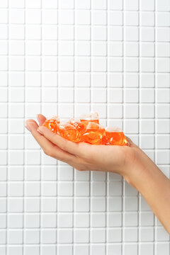 Hand holding vibrant orange laundry capsules