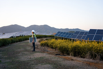 Engineer holding a solar panel while inspecting a mountainous photovoltaic power station at dusk © zhu difeng