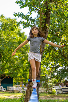 Cute little girl balancing on slackline outdoors. Active child enjoying outdoor activity during vacation. Concept of childhood, balance training, fun, healthy lifestyle.