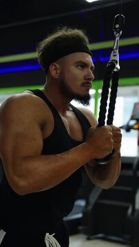 Focused athlete performs cable triceps pushdowns in a modern gym, showcasing muscular arms and disciplined form with a rope attachment during an intense strength workout.