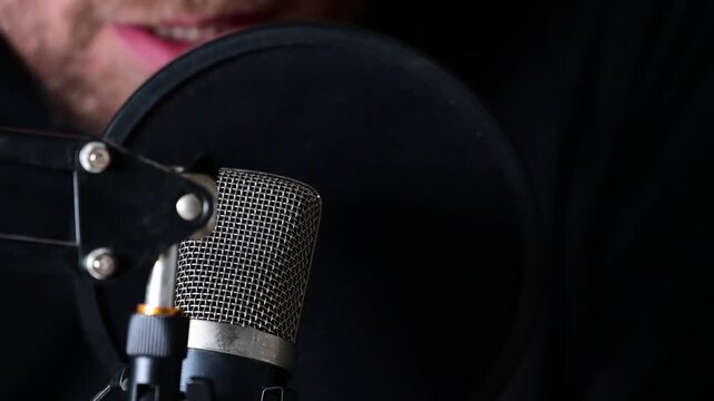 talking to podcast microphone close up, dark background selective focus video, close up on the microphone with mans lips moving, talking.