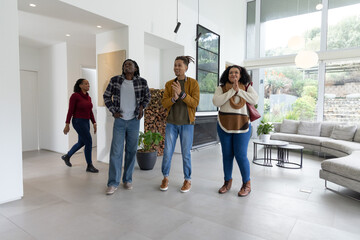 Fototapeta premium African American friends walking into modern living room, clapping near fireplace and windows