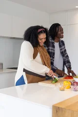 Fotobehang Koken African American couple preparing meal in modern kitchen slicing cucumber on wooden board  © wavebreak3