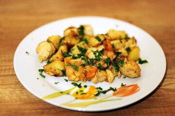 Close-up of pan roasted chicken and golden potatoes topped with fresh parsley, served on white floral plate over wooden table with shallow depth of field, 26 Feb. 2026