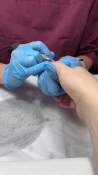 Nail technician in gloves removes old gel coat with e-filing, close-up view on hands. Specialists in hand and foot care, beauty salon, spa. Manicurist profession. Hands grooming and care